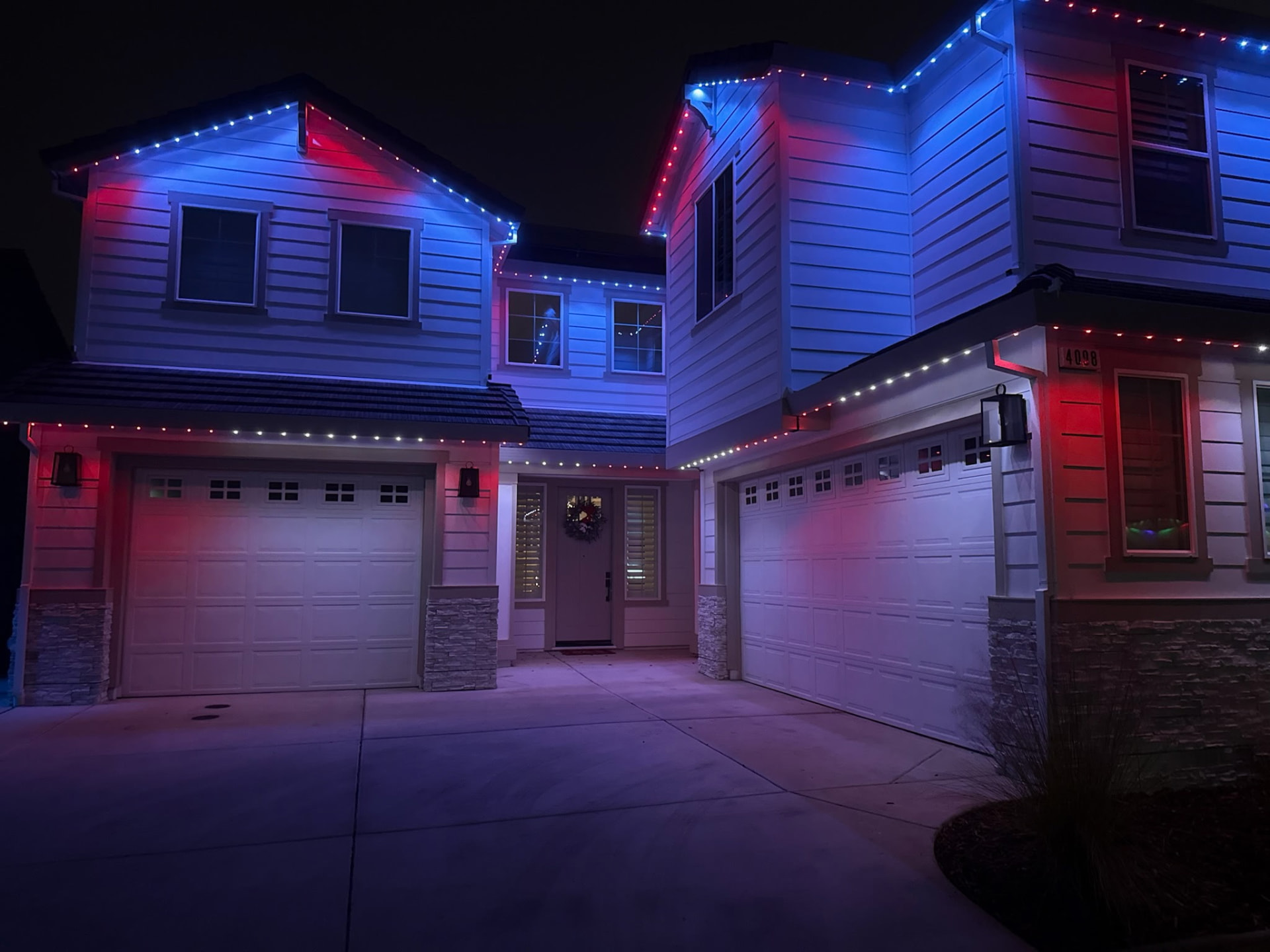 Red and blue permanent lighting along the roofline of a modern two-story home at night